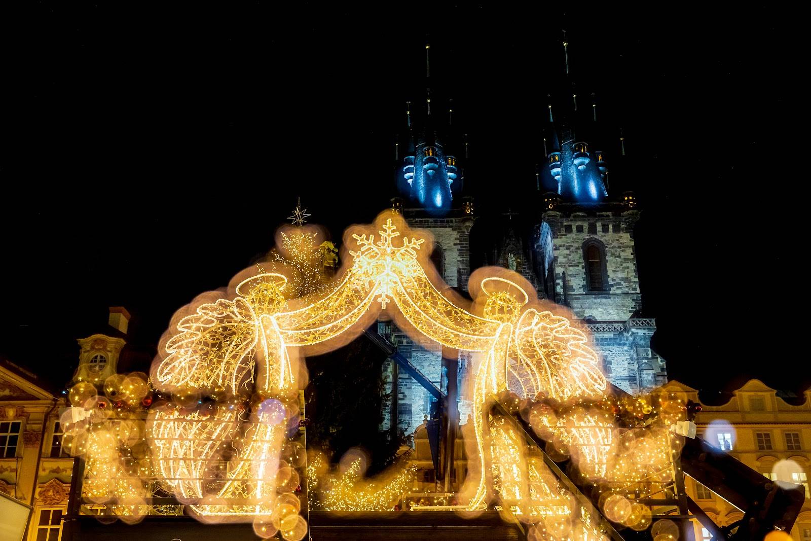 Sfeervolle eindejaarsverlichting in de vorm van engelen op een historisch stadsplein bij nacht.